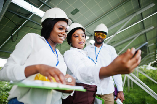 African american technician checks the maintenance of the solar panels. Group of three black engineers meeting at solar station. Make selfie by phone.